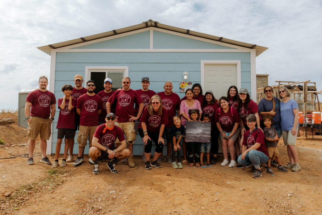 Morales Group team stands next to family outside of newly build home. This is project alongside YWAM Homes of Hope ministry.